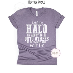 May include: A heather purple t-shirt with the text "hold my HALO I'M ABOUT TO DO UNTO OTHERS AS THEY HAVE DONE unto me" printed in white.