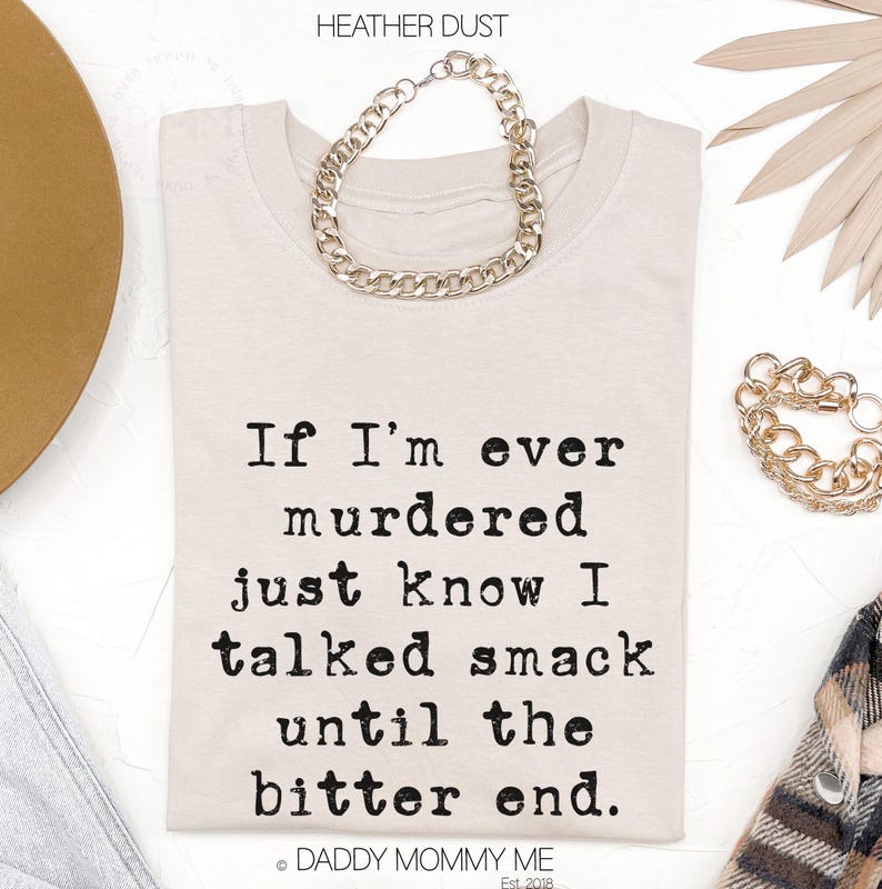 K&ouml;nnte beinhalten: Cremefarbenes T-Shirt mit dem Text "If I'm ever murdered just know I talked smack until the bitter end." Eine silberne Kette liegt &uuml;ber dem Shirt. Der Markenname "DADDY MOMMY ME" steht unten.
