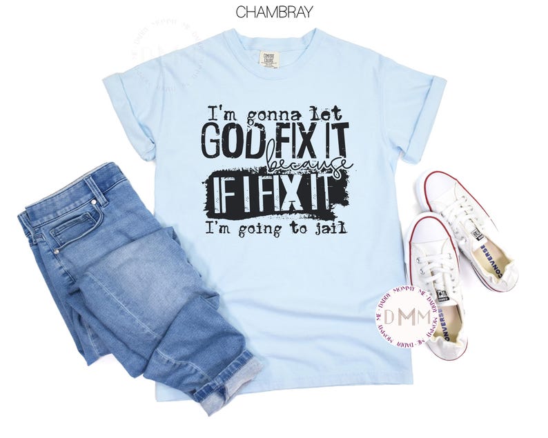 May include: A light blue short-sleeve t-shirt with black text that reads: I'm gonna let GOD FIX IT because IF I FIX IT I'm going to jail. The shirt is paired with blue denim jeans and a pair of white low-top canvas sneakers with white laces.