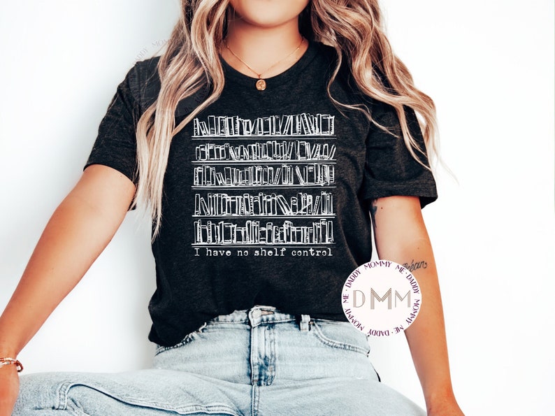 May include: A dark gray t-shirt with a white graphic of a bookshelf full of books. The text "I have no shelf control" is printed below the graphic.