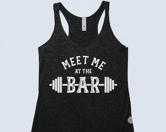 May include: Dark gray racerback tank top with the text "MEET ME AT THE -BAR-" in white. The word "BAR" is designed to look like a barbell. A casual athletic top for workouts or everyday wear.