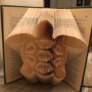 May include: A book folded into the shape of a sea turtle. The book is open and the pages are folded to create the shape of the turtle's shell. The turtle is facing the right side of the image.