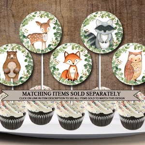 May include: Six cupcake toppers featuring woodland animals. The toppers are round and have a white background with green leaves around the edge. The animals include a deer, a raccoon, a bear, a fox, an owl, and a squirrel. The toppers are perfect for a woodland-themed party.