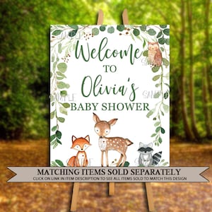 May include: Welcome to Olivia's Baby Shower sign with a green leafy border and woodland animal illustrations. The sign features a fox, a deer, a raccoon, and an owl.