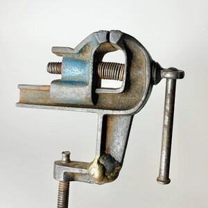May include: A vintage metal vise with a blue and gray finish. The vise has a movable jaw and a handle for tightening.