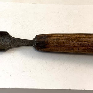 Op de afbeelding: Een vintage beitel met een houten handvat en een metalen blad. De beitel heeft een metalen band om het handvat.