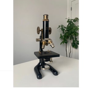 May include: A vintage black microscope with brass accents. The microscope has two eyepieces and a stage for viewing slides.