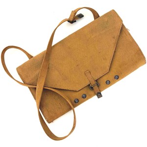 May include: A tan canvas messenger bag with a long shoulder strap. The bag has a flap closure secured by a buckle and several metal snap closures. The bag is made of a durable, textured fabric.