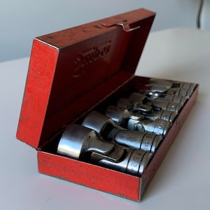 May include: A red metal box containing a set of 8 silver socket wrenches. The box is labelled "Snap-on" and the wrenches are labelled with sizes.