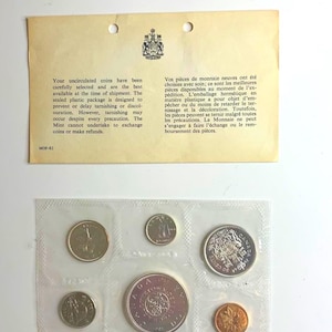 May include: A white ceramic mug with a black handle and the text "But First, Coffee" in a bold, black font. The mug is set against a blurred background, suggesting a cosy setting.