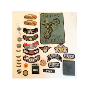 May include: A collection of Harley Davidson motorcycle patches, pins, and other memorabilia. The patches feature the Harley Davidson logo, the HOG logo, and the words "Loud Pipes Save Lives". There is also a patch that says "1st C.A.V. Canadian Army Veteran".