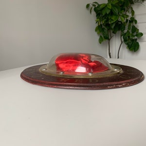 Peut inclure: Une bo&icirc;te en velours rouge en forme de c&oelig;ur avec un couvercle en plastique transparent, pos&eacute;e sur une base en bois avec le mot "RED" imprim&eacute; dessus.
