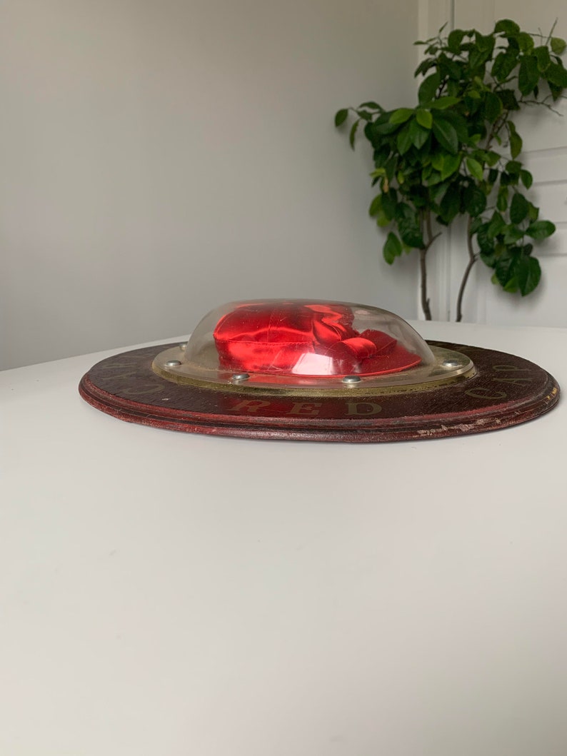 Peut inclure: Une bo&icirc;te en velours rouge en forme de c&oelig;ur avec un couvercle en plastique transparent, pos&eacute;e sur une base en bois avec le mot "RED" imprim&eacute; dessus.
