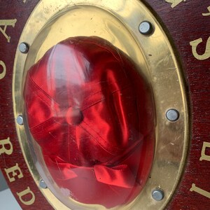 Peut inclure: Une casquette de baseball en satin rouge est expos&eacute;e dans un cadre circulaire en bois avec une bordure en m&eacute;tal dor&eacute;. Le cadre porte les mots "CARDINAL" et "AIR".