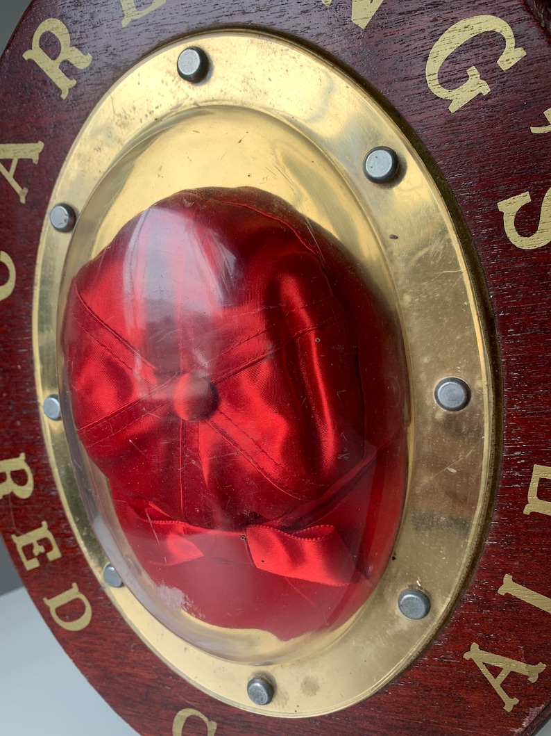 Peut inclure: Une casquette de baseball en satin rouge est expos&eacute;e dans un cadre circulaire en bois avec une bordure en m&eacute;tal dor&eacute;. Le cadre porte les mots "CARDINAL" et "AIR".