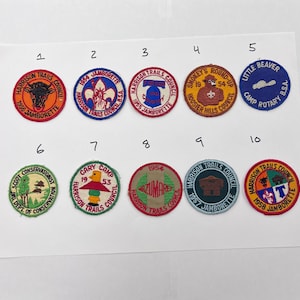 Puede incluir: Una colección de diez parches bordados vintage. Cada parche presenta un diseño circular con texto e ilustraciones, incluyendo un toro, una flor de lis y un castor. Los parches son de varios colores, incluyendo rojo, azul y naranja.