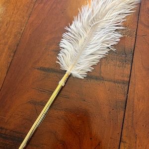 May include: A white ostrich feather pen with a gold metal body and a decorative beaded accent.