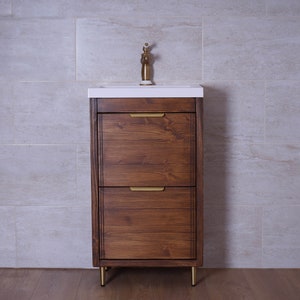 May include: A brown wooden bathroom vanity with two drawers and gold hardware. The vanity has a white countertop and a gold faucet. The vanity is standing on four gold legs.