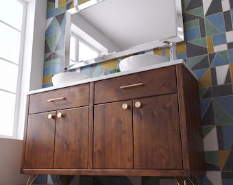 Puede incluir: Un mueble de baño doble de madera marrón oscuro con herrajes dorados, que cuenta con dos lavabos sobre encimera blancos sobre una encimera blanca, apoyado sobre patas de horquilla doradas, bajo un espejo rectangular con marco plateado.