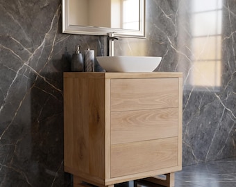May include: A light oak bathroom vanity cabinet featuring three horizontal drawers with a natural wood grain finish, supported by a rectangular base frame, topped with a white oval vessel sink and a silver faucet fixture.