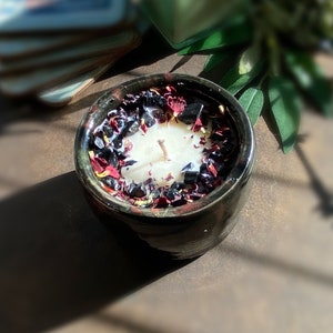 May include: A black ceramic candle holder with a white candle and dried red and black flower petals.
