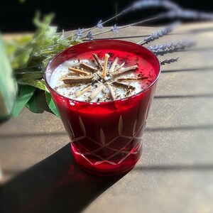May include: A red glass candle holder with a white candle and a wooden star-shaped design on top. The candle holder has a diamond pattern.
