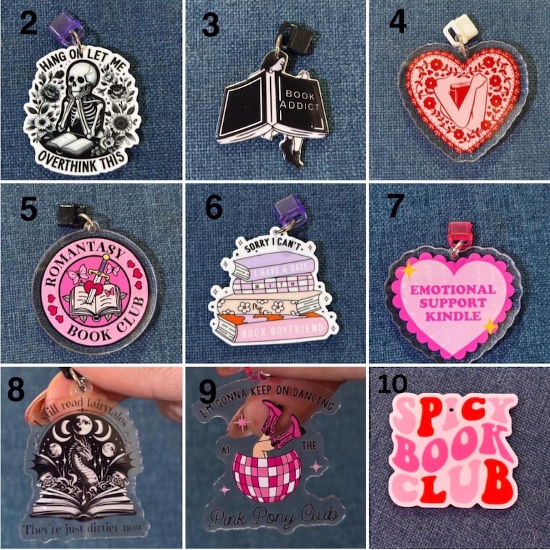 May include: A collection of acrylic charms with various book-themed designs. The charms feature phrases like "Book Addict," "Romantasy Book Club," and "Emotional Support Kindle." Colors include pink, black, white, and red. Some charms have text, and others feature illustrations.