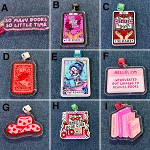May include: A collection of acrylic keychains with book-themed designs. The keychains feature various quotes and illustrations, including a stack of books, a tarot card, and the text "So Many Books So Little Time."