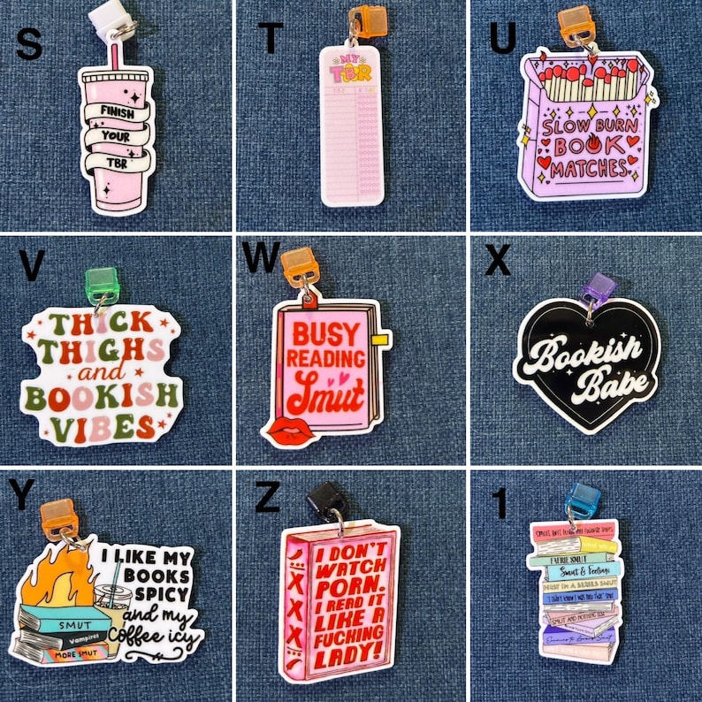 May include: A collection of colorful, whimsical book charms with various designs and text. The charms include a pink drink with text, a pink TBR list, a matchbox with text, a heart-shaped charm with text, a charm with text and a book, a charm with text and a stack of books, and a charm with text and a book with a lip.