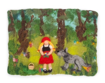 Op de afbeelding: Een wandkleed van vilt dat een scène uit Roodkapje voorstelt. Een meisje in een rode kapmantel en een mand met bloemen staat in een groen bos met een grijze wolf.