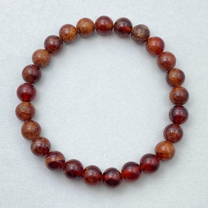May include: A red gemstone bracelet with round beads. The beads have a mottled, brown and red appearance.