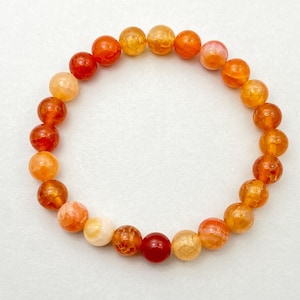 Op de afbeelding: Een armband gemaakt van oranje, gele en rode agaat kralen. De kralen zijn rond en hebben een natuurlijke, getextureerde afwerking.