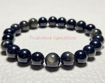 Könnte beinhalten: Ein schwarzes Edelstein-Armband mit goldenen Flecken in den Perlen. Das Armband besteht aus runden Perlen und ist auf einem Gummiband aufgefädelt.