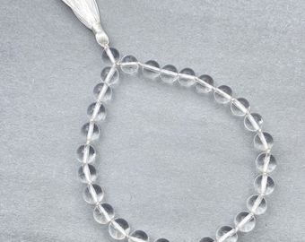 Op de afbeelding: Een mala-ketting van heldere kristallen kralen met een witte kwast.