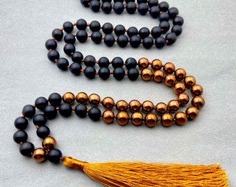 May include: A black and copper beaded necklace with a gold tassel. The necklace is made of round beads and has a two-tone design.