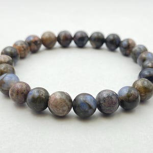 Könnte beinhalten: Ein Armband aus dunkelblauen, braunen und grauen Edelsteinperlen. Die Perlen sind rund und haben ein gesprenkeltes Muster.