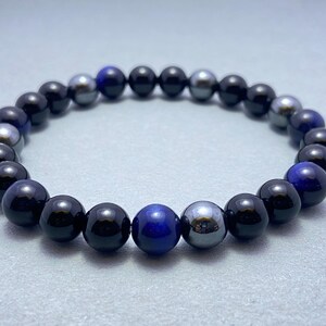 May include: A beaded bracelet with black, blue, and silver beads. The bracelet is made of round beads and has a simple design.
