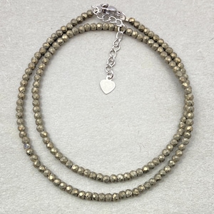 Puede incluir: Un collar de doble cadena hecho de pequeñas cuentas doradas facetadas. El collar tiene un dije de corazón plateado y un cierre de langosta plateado.