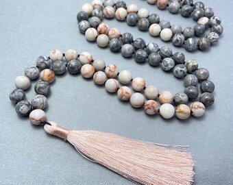 May include: A long gray, white, and orange stone bead necklace with a pink tassel.