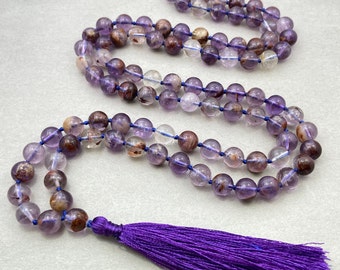 May include: A purple amethyst mala with a purple tassel. The beads are clear with a purple hue and have brown and gold inclusions. The mala is made of 108 beads and is approximately 54 inches long.