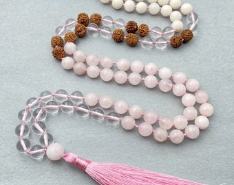 May include: A pink and white mala necklace with a pink tassel. The necklace is made of clear quartz, rose quartz, and rudraksha beads.