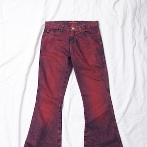 May include: A pair of red and purple flared jeans. The jeans have a classic five-pocket design with a button and zip closure. The fabric has a faded, distressed look, with a gradient effect from red to purple.