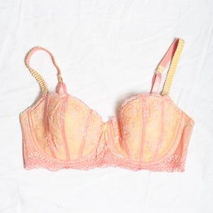 Puede incluir: Un sujetador de encaje delicado de color rosa y amarillo con tirantes ajustables.