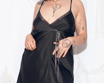 May include: A black satin slip dress with a lace trim and a tie at the waist.