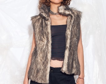 May include: A brown and white faux fur vest with a black and white striped tank top underneath. The model is wearing black pants and white sunglasses.