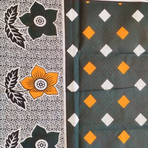 May include: A fabric with a black and white floral pattern on one side and a green background with orange and white diamond shapes on the other side.