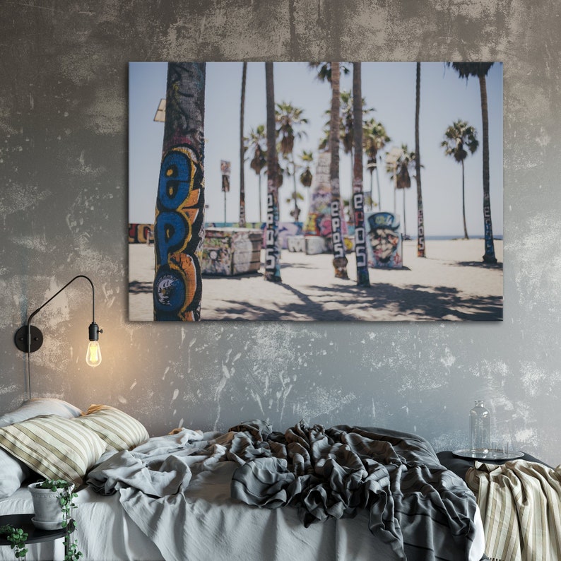 Peut inclure: Une photographie d'une sc&egrave;ne de plage avec des palmiers et des graffitis sur les troncs. Les graffitis sont de couleur bleue, jaune et rouge. La plage est sablonneuse et le ciel est bleu en arri&egrave;re-plan.