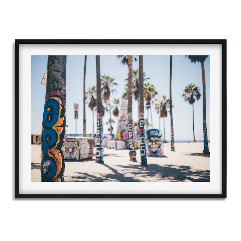 Peut inclure: Gros plan sur des troncs de palmiers peints de graffitis color&eacute;s sur une plage. Les troncs sont nets, tandis que l'arri&egrave;re-plan est flou.