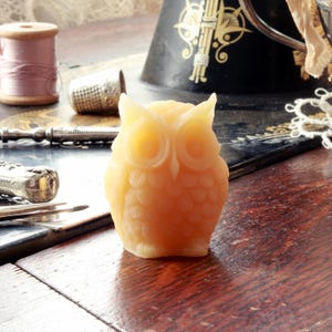May include: A small, yellow, owl-shaped candle. The candle is made of beeswax and has a detailed design.