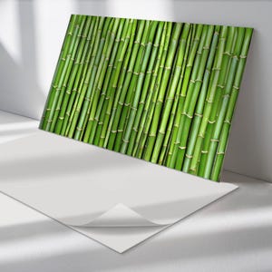 May include: A vibrant green bamboo print on a rectangular canvas. The bamboo stalks are arranged diagonally, creating a textured pattern. The artwork is leaning against a white wall, with a white sheet of paper in the foreground.
